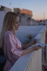 Fototapeta premium Woman enjoying morning coffee on an urban rooftop terrace, finding peace and quiet during self-care relaxation at dawn, embracing a serene routine