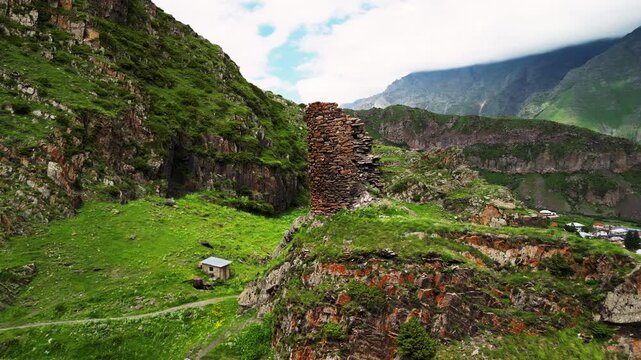 Cinematic 4K ProRes 422 aerial orbit of ancient tower ruins on a cliff. Mystical green ravine with a mountain river in Georgia.