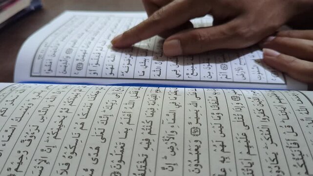 Person pointing finger at holy quran pages open reading sacred islamic text close up motion footage learning prayer scripture calligraphy reciting.