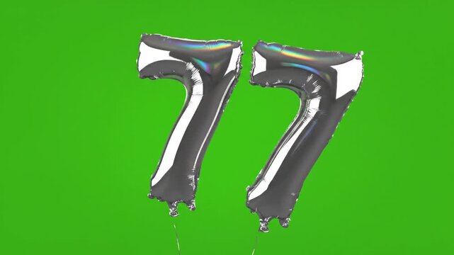 Silver metallic number 77 balloons floating against a vivid green background for celebration