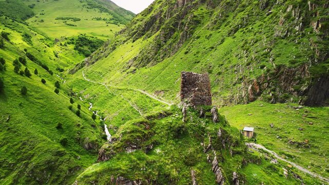 Cinematic 4K ProRes 422 aerial orbit of ancient tower ruins on a cliff. Mystical green ravine with a mountain river in Georgia.