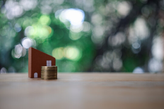 Mini toy home with coin stacks symbolizing real estate investment against nature background