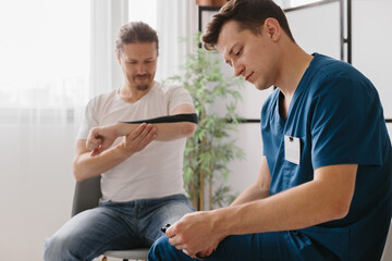 Fototapeta premium Orthopedic doctor treating a patient's arm with kinesiology tape.
