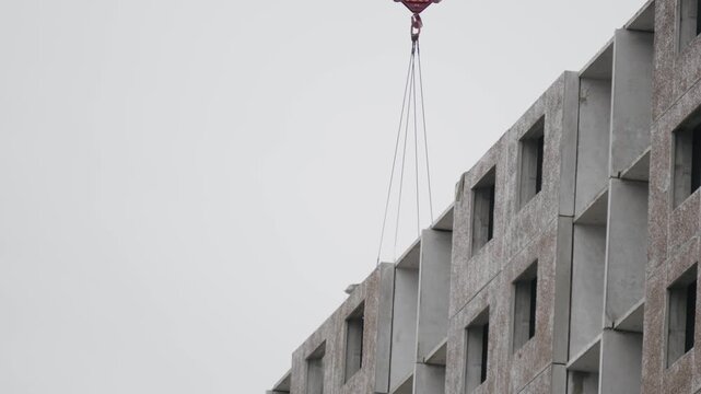 Construction site machinery. Building highrise with textured panel installation. Heavy equipment elevates precast slabs on construction zone