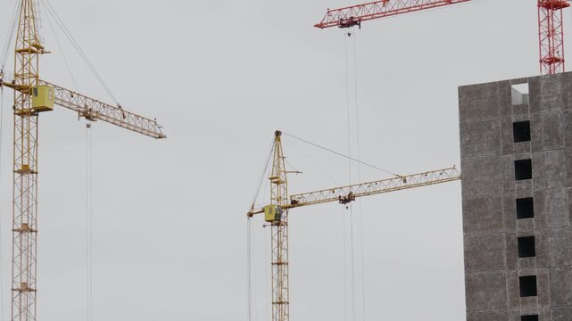Crane operation above incomplete structure under cloudy sky. Urban development scene showing cranes and concrete core against overcast sky mood