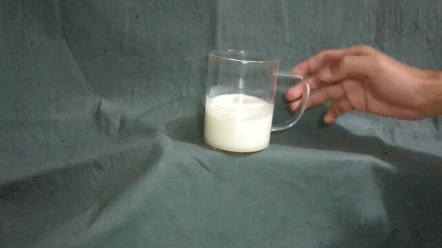 Hand places glass mug with white liquid onto textured surface close up shot cinematic motion.