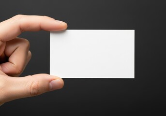 Obraz premium Close up of a hand holding a blank white business card against a dark gray background