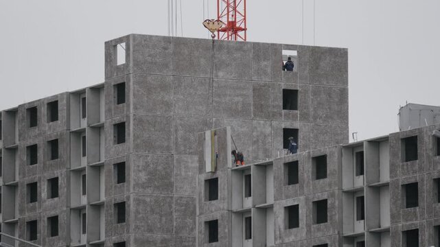 Building facade assembly. Construction crew carefully places precast sections on multilevel facade using safety harnesses and mobile crane