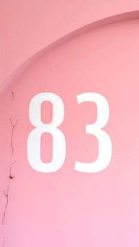 An architectural detail showcases the white number "83" on a pastel-pink wall with a subtle arched structure. A crack is visible