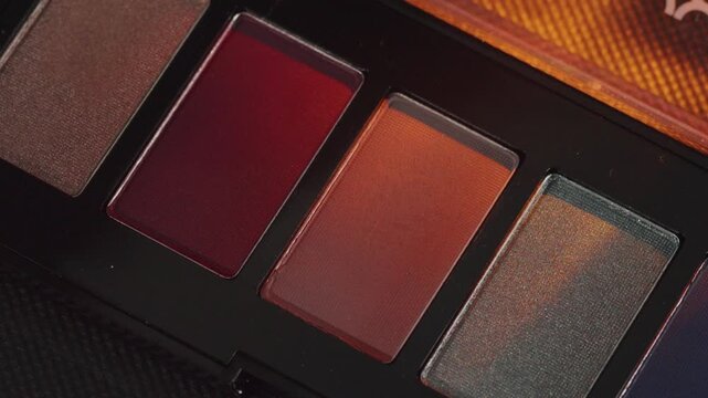 Closeup eyeshadow palette warm orange red cinematic amber tones, threepan compact, matte and shimmer mix, textured surface, editorial beauty lighting