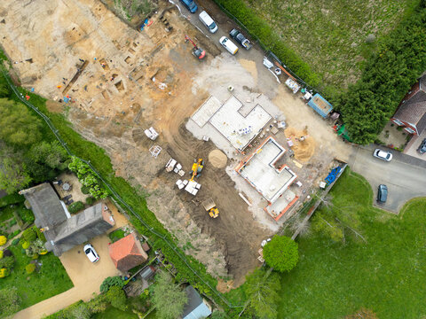 Done UAV view of a small housing development seen within rural Britain. The foundations of two bungalows can be seen, adjacent to some existing housing.