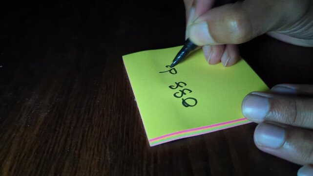Person writing 088 day on yellow sticky note with black marker on wooden desk under focused lighting during evening study session at home office recording professional high quality video footage.