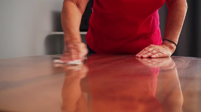 A person uses a cloth to wipe a round black mat placed on a wooden table.