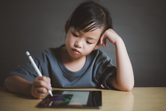 Little Asian girl using tablet and stylus for remote learning at home