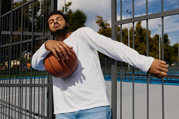 Young man showcasing basketball skills on an outdoor court under a clear blue sky © LIGHTFIELD STUDIOS