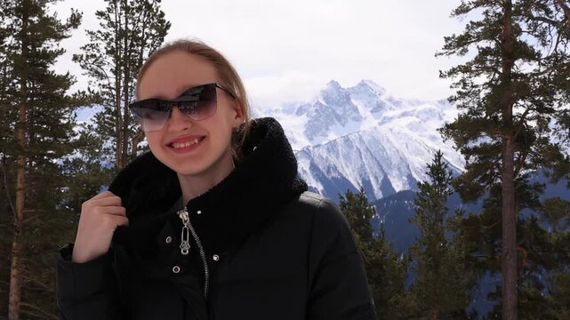 A girl on the top of a snow-capped mountain in a leather jacket and sunglasses.