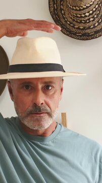 Vertical video: Reaching man in teal shirt in hall taking Panama hat off peg, checking fit, hats