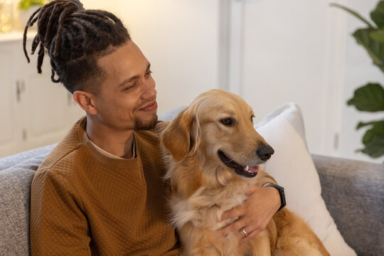 Man sitting on sofa in living room holding golden retriever on lap, wearing brown quilted sweater