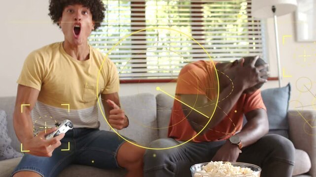 Vertical video: Cheering postgame yellow tee and sulking orange tee home on sofa with pads popcorn