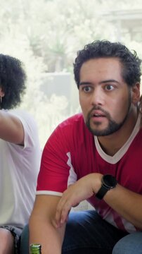 Vertical video: Viewing man in red jersey fidgeting green bottle at home, lunging after team scores