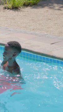 Vertical video: Splashing teen wearing red swim trunks cooling off in sun at home pool, copy space
