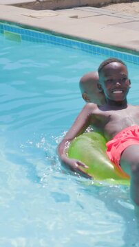Vertical video: Helping dad steadying son in red trunks boarding green tube at pool, learning swim