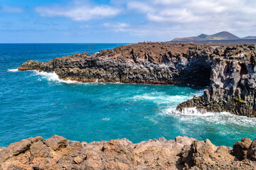 Lava cliffs at Los Hervideros with Atlantic Ocean, waves and rugged rocks under blue sky on Lanzarote.