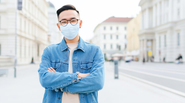 Young Asian man wearing a medical mask and eyeglasses feeling protected standing on an urban street