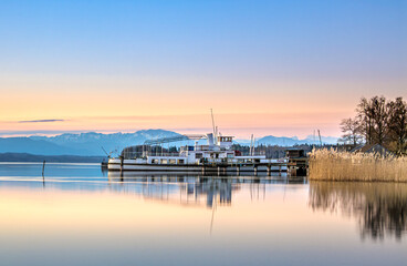 Obraz premium Altes stillgelegtes Ausflugsschiff an einem Holzsteg spiegelt sich im klaren Wasser im Morgenlicht am Starnberger See, Tutzing, Bayern, Deutschland Europa
