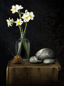 still life with flowers, rounded stones, and seed pod of sweetgum tree on old wooden box