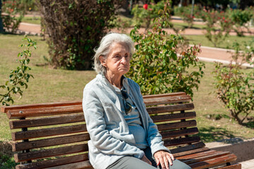Fototapeta premium An 85 year old grandmother sits alone on a park bench enjoying a sunny day