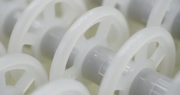 An industrial conveyor is in operation, white plastic rollers are rotating. Static handheld shot of production, sorting, or transportation line, real time speed, artificial lighting.