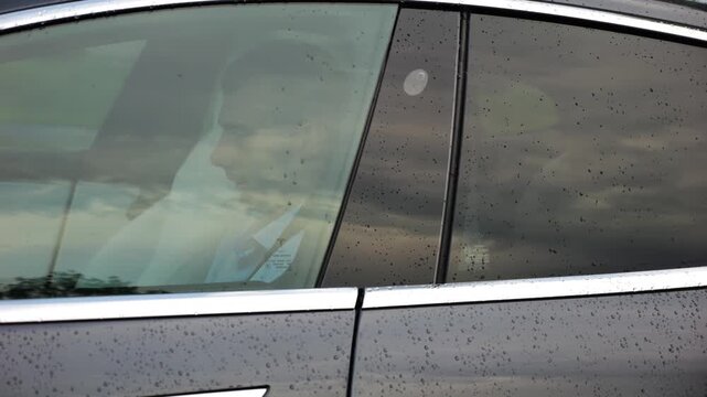 Young entrepreneur work on notebook while riding an autonomous self driving electric car at urban road. Male businessman type text on laptop during ride on electrical vehicle with autopilot after rain