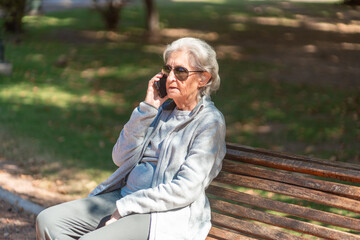 Fototapeta premium An 85-year-old grandmother enjoys a phone call while sitting on a park bench