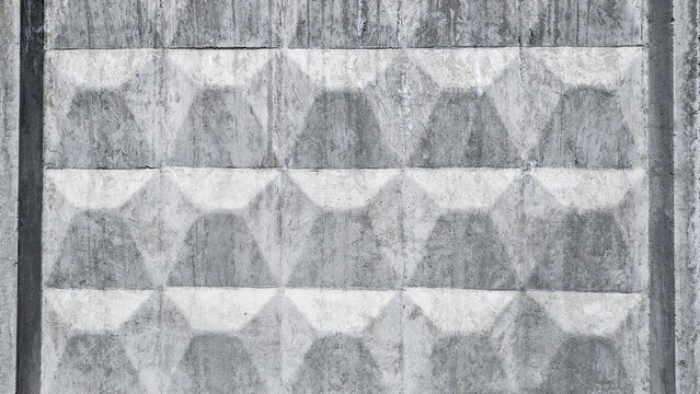 Gray precast concrete fence panel revealing a textured diamond pattern with strong shadows and rough surface details, representing brutalist architecture and urban industrial design