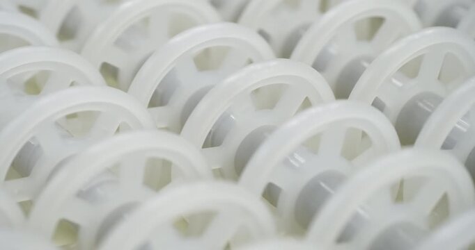 An industrial conveyor is in operation, white plastic rollers are rotating. Static handheld shot of production, sorting, or transportation line, real time speed, artificial lighting.