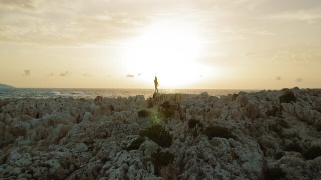 Female standing on rocky cliffside overlooking ocean in Kefalonia during sunset