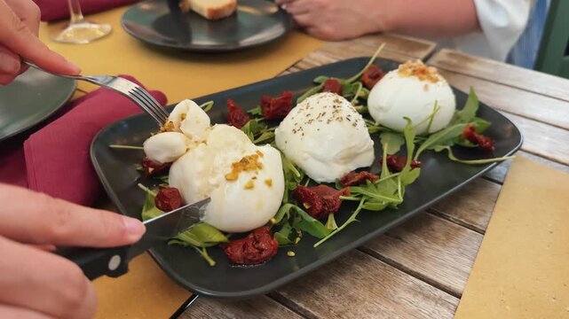 A woman cuts cheese with a knife in a cafe on a black plate. Three types of cheese from the Italian provinces. Traditional dishes of Rome