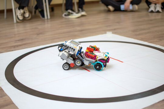 Robot Testing on White Vinyl Field with Human Feet in Background. An experimental robotic device performing a task on a marked testing area with a supervisor standing nearby.