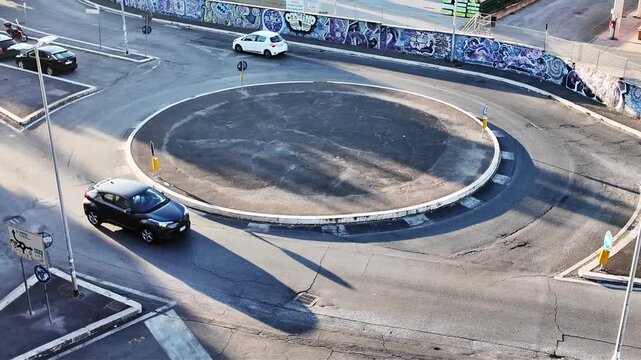 Cars navigate a bustling roundabout with vibrant murals on the surrounding walls during a sunny day