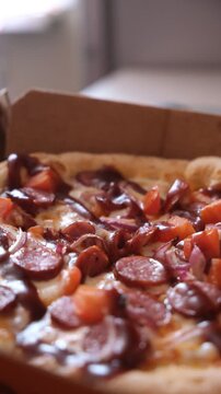 Spicy pizza with chorizo sausages, pelati sauce, mozzarella cheese topped with salami, smoked chicken, garnished with fresh tomatoes and red hot pepper slices. Cardboard box