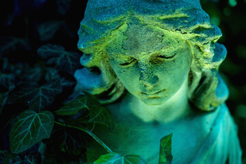 Fototapeta premium Angel statue with ivy in cool green light, mystical concept of silence, eternity and spiritual peace.