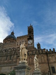 Obraz premium Palermo Cathedral featuring ornate architecture, clock tower, and statues in the foreground against a clear blue sky in Palermo, Sicily, Italy