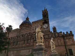 Obraz premium Palermo Cathedral with clock tower and statues in foreground, showcasing intricate architecture and historical details against a blue sky in Palermo, Sicily, Italy