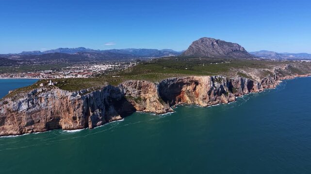 Cabo de San Antonio cape in Alicante Spain showing 175-meter high limestone cliffs, white lighthouse, turquoise Mediterranean Sea and Montgo mountain in background
