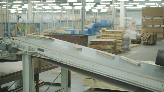 A neat stack of wooden boards on a pallet with a blurred person operating an automated line in the background