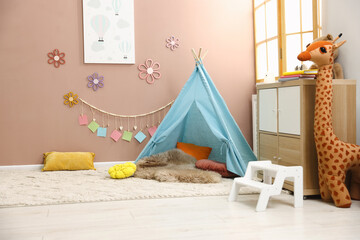 Colorful paper notes and beautiful decor hanging on beige wall near toy wigwam in stylish children's room. Interior design © New Africa