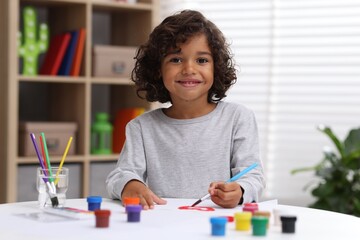 Cute little boy painting on paper with paints and brush at white table indoors © New Africa