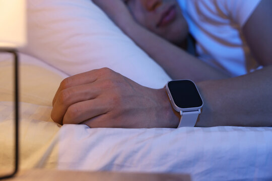 Young man with sleep tracker sleeping on bed at home, closeup