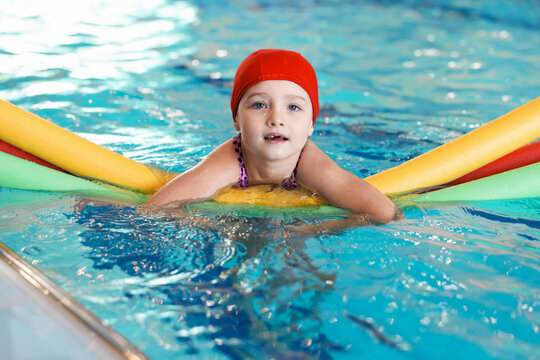 Cute little girl swimming with water noodles during lesson in pool